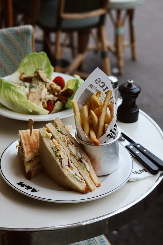 Club sandwich au poulet, cornet de frites et salade sur une table du café